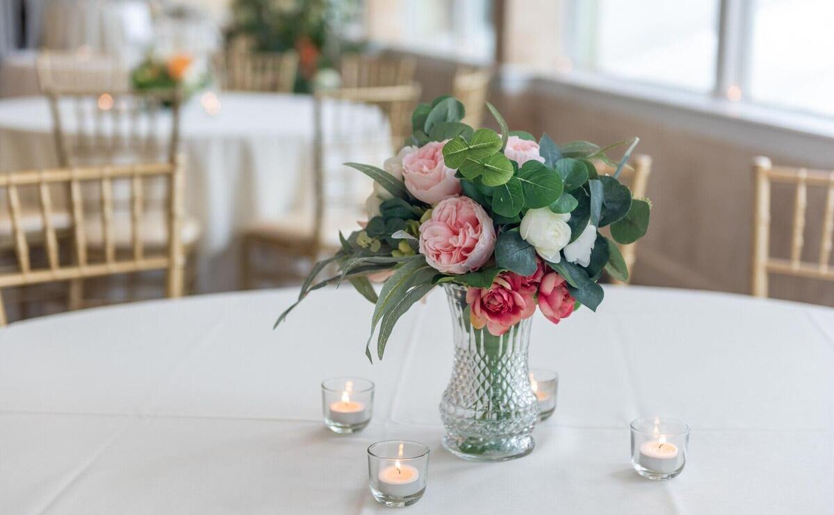 Closeup shot of a bouquet of elegant flowers in a glass vase surrounded by candles on the table