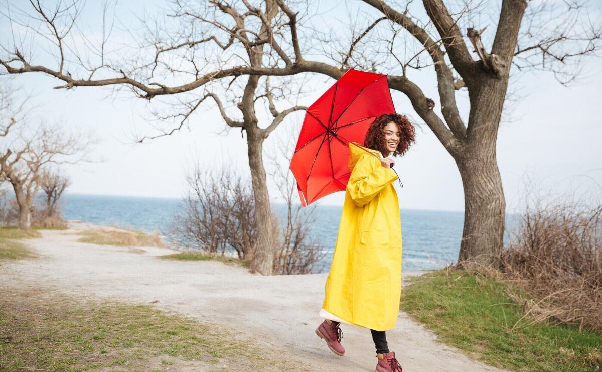 Happy african curly young lady wearing yellow coat holding umbrella