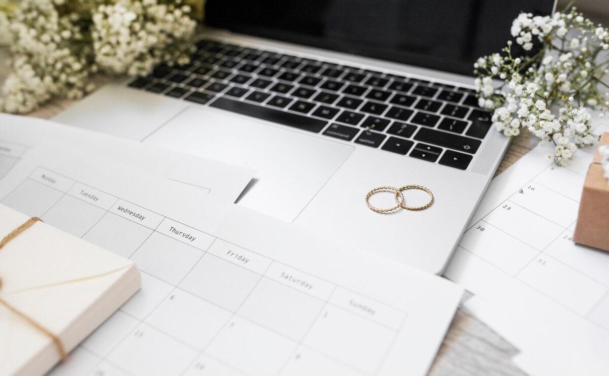 Close-up of calendar; wedding rings; baby's-breath flowers and laptop on desk