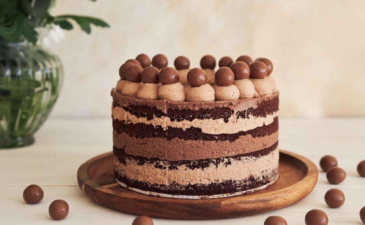 Vertical shot of a delicious chocolate naked cake with choco balls and cream on a white table