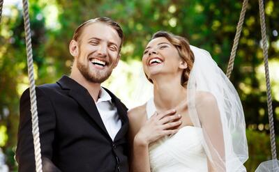 Young beautiful newlyweds smiling, laughing, sitting on swing in park.