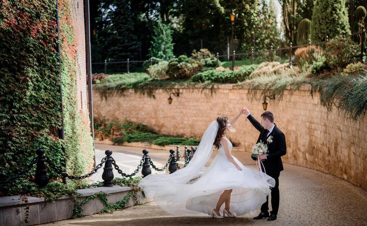 Wedding couple is dancing near stone wall covered with green ivy