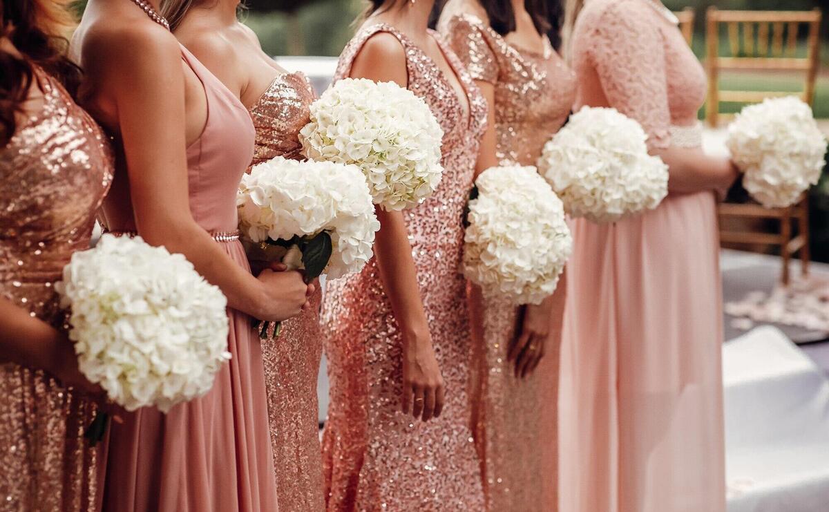 Bridesmaids in pink dresses stand with white flower bouquets in