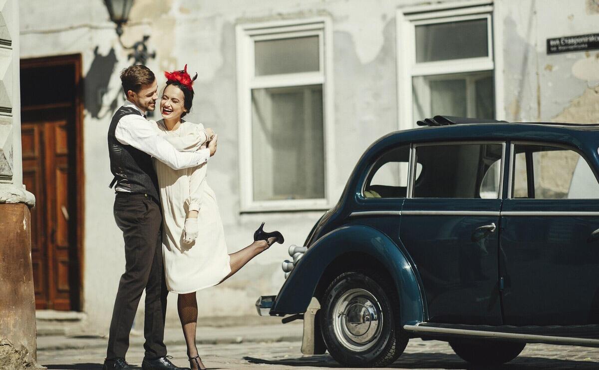 Lovely couple dressed in 30's style hugs on the street standing before an old car