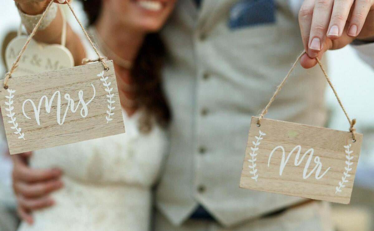 Happy newlyweds hold wooden boards with letterings 'mrs' and 'mr'